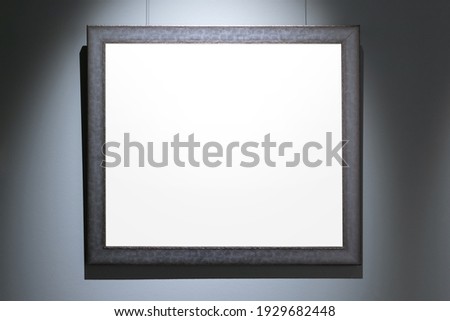Black wooden frame with blank white copy space area is on blue wall. Front view, background photo