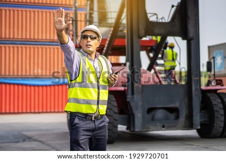 Young male engineer or manager wearing safety helmet and making hand to stop while talking on walkie talkie, transport and logistics concepts