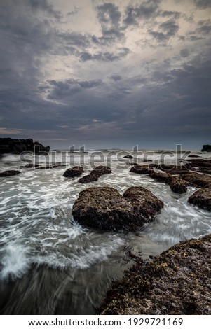 Beautiful seascape for background. Beach with rocks and stones. Low tide. Motion water. Cloudy sky. Slow shutter speed. Soft focus. Copy space. Vertical layout. Mengening beach, Bali, Indonesia