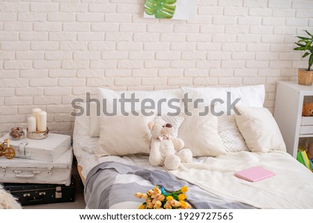 cozy bed with light linens and a teddy bear and a knitted blanket made of merino yarn. Bright bedroom with lots of indoor plants and home decor.The concept of home comfort and relaxation.
