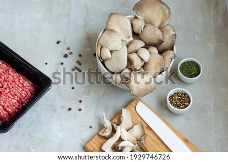 Mince meat in the beige bowl, oyster mushrooms, seasonings on the light grey background