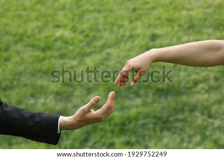 Close-up blurred female and male fingers touching each other in front of grass ground background