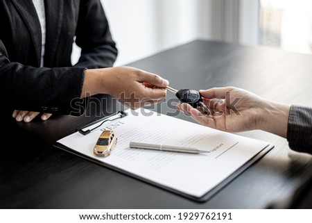 A car rental company employee is handing out the car keys to the renter after discussing the rental details and conditions together with the renter signing a car rental agreement. Concept car rental.