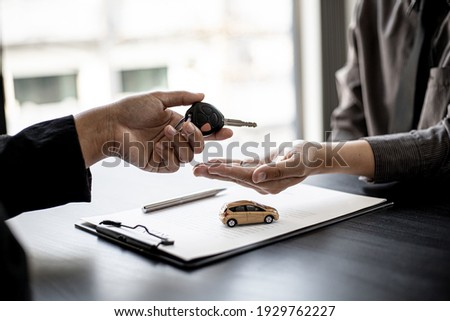 A car rental company employee is handing out the car keys to the renter after discussing the rental details and conditions together with the renter signing a car rental agreement. Concept car rental. Royalty-Free Stock Photo #1929762227