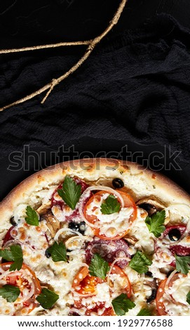 pizza on black textured background with dark napkin and golden sprigs top view