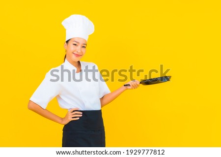 Portrait beautiful young asian chef woman with black pan on yellow isolated background
