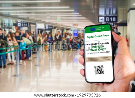 The digital green pass of the european union with the QR code on the screen of a mobile held by a hand with blurred airport in the background. Immunity from Covid-19. Travel without restrictions. Royalty-Free Stock Photo #1929795926