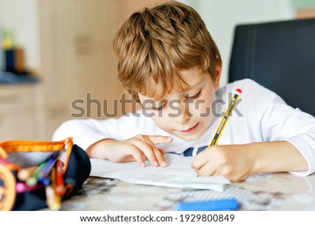 Hard-working school kid boy making homework during quarantine time from corona pandemic disease. Child on home schooling in coronavirus covid time, schools closed. Homeschooling concept Royalty-Free Stock Photo #1929800849