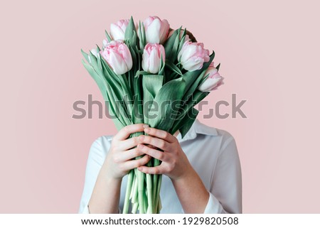 A girl covering her face with a bunch of pink tulip flowers