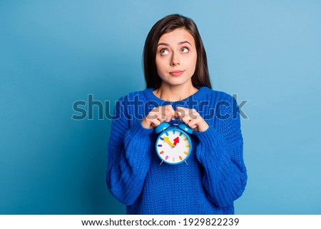 Photo of young attractive thoughtful dreamy charming girl thinking look copyspace hold clock isolated on blue color background