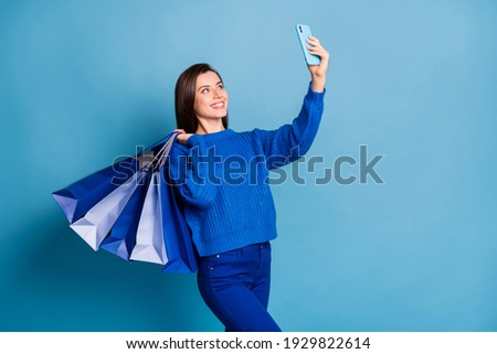 Photo of young happy positive lovely good mood girl hold shopping bags take selfie on phone isolated on blue color background