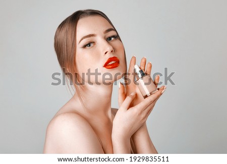 Woman holds hyaluronic serum. Photo of attractive woman with nose earring, red lips and perfect makeup on gray background. Beauty concept