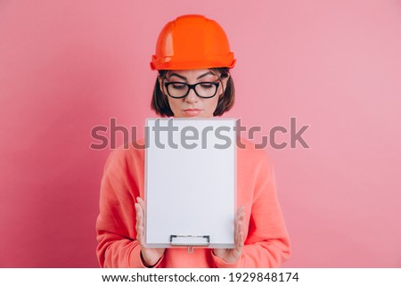 Pretty woman worker builder hold white sign board blank against pink background. Building helmet. 