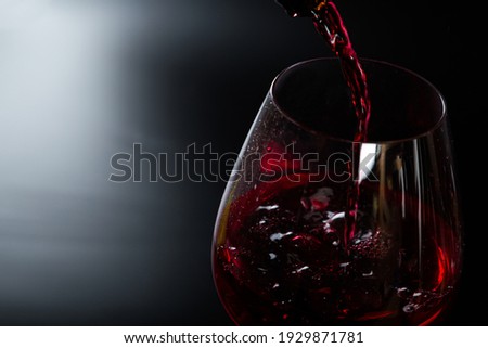 Pouring red wine into a glass on a black background. splashes and drops