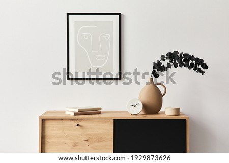 Stylish interior of living room with mock up poster frame, wooden commode, book, eucalyptus leaf in ceramic vase and elegant personal accessories. Minimalist concept of home decor. Template.