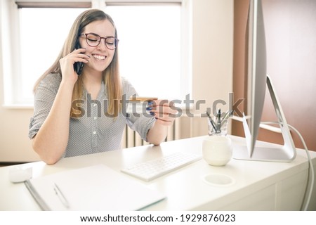  young woman with glasses, working from home using smart phone and computer, woman's hands using smart phone in interior, at home workplace using technology, credit card. High quality photo
