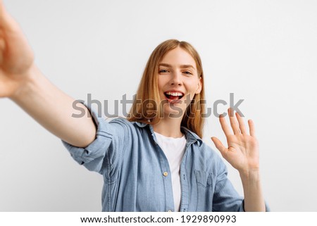 Young happy woman taking light cheerful selfies and waving hi on white background