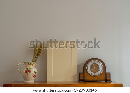 close up of still life  mock up beige picture mount, antique timber clock with floral jug and wheat rye floral arrangement
