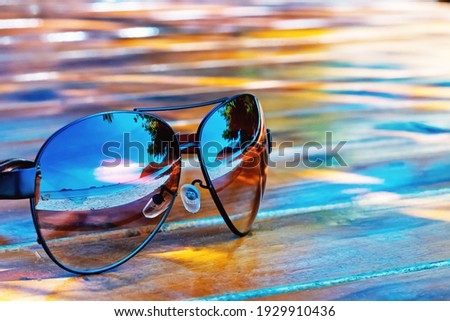 The sunglasses lie on a wooden surface that reflects the seascape. Copy space. 

