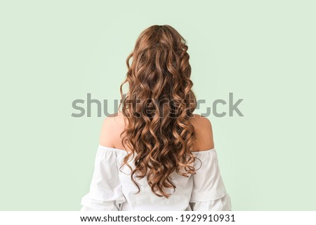 Beautiful young woman with stylish hairdo on color background, back view Royalty-Free Stock Photo #1929910931