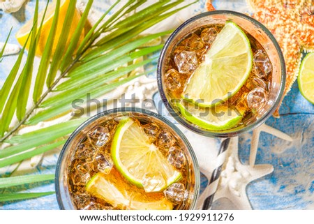 Summer holiday vacation tropical background with iced beverages. Cuba Libre, long island iced tea cocktail with strong alcohol, cola, lime, crushed ice, tropical background with starfish, palm leaves 