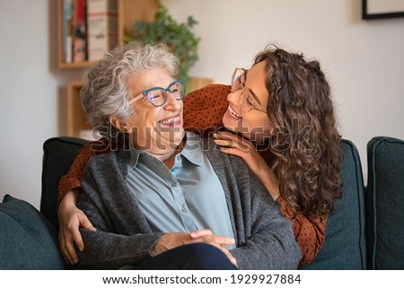 Old grandmother and adult granddaughter hugging at home and looking at each other. Happy senior mother and young daughter embracing with love on sofa. Happy woman hugging from behind grandma with love Royalty-Free Stock Photo #1929927884