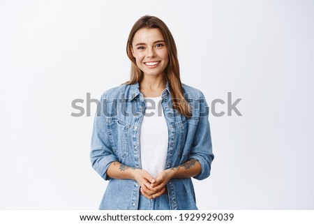 How may I help you. Smiling young woman with fair hair holding hands together and looking friendly at camera, happy emotions, white background