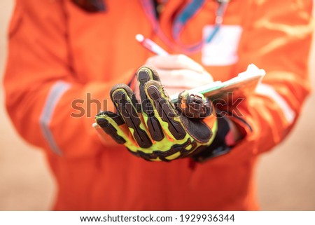 Close-up action of safety supervisor's hand which is weared an impact glove is holding a clipboard, and use the another hand writing something on paper during safety audit. Selective focus at glove.  
