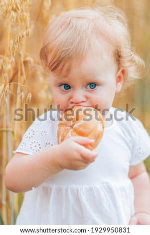 Close-up of a little girl drinking milk from a glass bottle, eating bread in a wheat field.