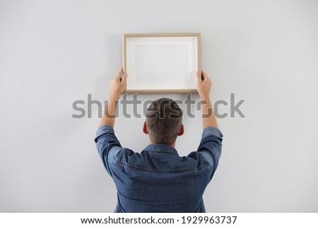 Man hanging picture on white wall indoors. Interior decoration