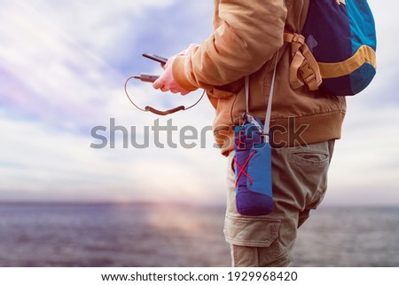 Man charges a smartphone with a portable charger. A man with a power bank in his hand on the background of the sea on a bright sunny day with clouds