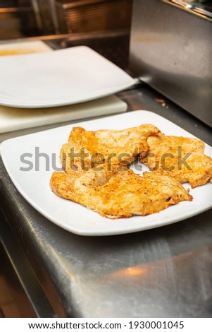 A view of a plate of seasoned chicken breast on the counter of a restaurant kitchen.