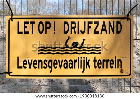 Yellow sign attached with cable ties on a wire mesh fence: Pay attention! Quicksand. Dangerous terrain ('Let op! Drijfzand. Levensgevaarlijk terrein' in Dutch)