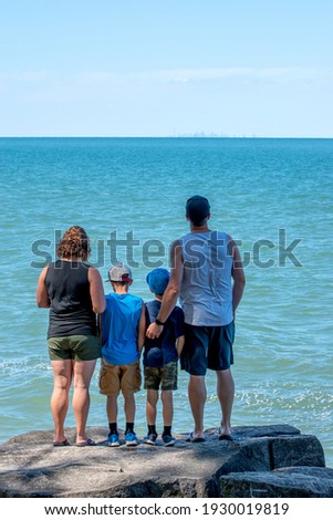 A family stands on the rocks on the shores of Lake Ontario looking out to the Toronto city skyline.