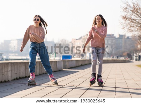 Two cute teenage girls on roller skates having fun in urban environment.