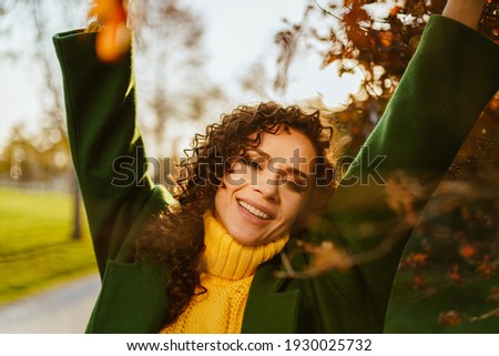 In the park against the background of crimson leaves curly brunette in autumn clothes sweetly stretches covering her eyes and smiling white-toothed smile. High quality photo