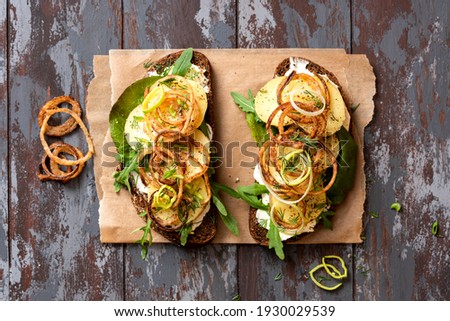 Sandwich with rye bread, butter, potatoes, sauce and crispy onions on a dark wooden background top view. Scandinavian cuisine. Easy and tasty lunch, dinner or beer snack. Free space for text. Rustic 