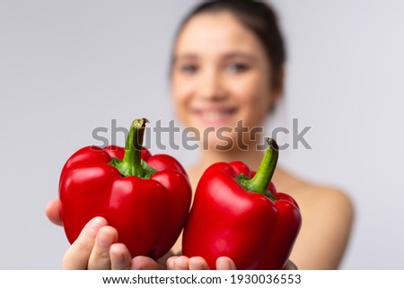 Blurred photo of a girl who stretches her hands to the camera while holding two large red, juicy sweet peppers. White background.