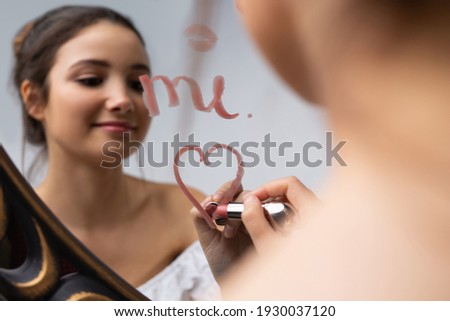 Blurred photo of a young girl posing in front of a mirror. Heart with lipstick on the mirror.