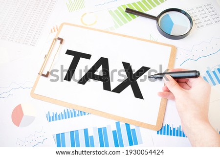 Text TAX on white paper sheet and marker on businessman hand on the diagram. Business concept