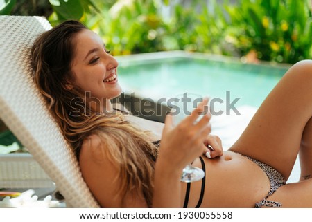 by the pool in a chair sits a girl with a glass in her hands and smiles tenderly. High quality photo