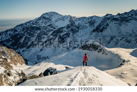 Ski tourer ascending a snow slope carrying skis on his backpack. Climber in a reed jacket climbs a mountain against a blue sky. On top of a mountain and enjoying view. Adventure concept Royalty-Free Stock Photo #1930058330