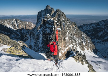 Skier on a mountain ridge in the winter, climbing towards the ice frosted peak. Mountaineer reaches the top of a snowy mountain in a sunny winter day.