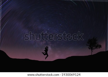 The silhouette of a tree and a woman jumping on a background full of spinning stars.
