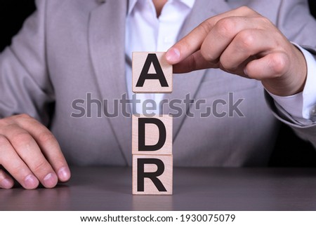 Alternative Dispute Resolution ADR, Adverse Drug Reaction, text written on wooden cubes against the background of a man in a gray suit sitting at a table. Royalty-Free Stock Photo #1930075079