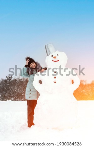 smiling woman makes a snowman on a winter day in a snow-covered field under the open sky. Artistically colored and tinted photography