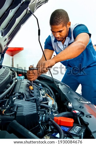 Horizontal shot of an automotive technician working on a car engine.  This is a revised picture.