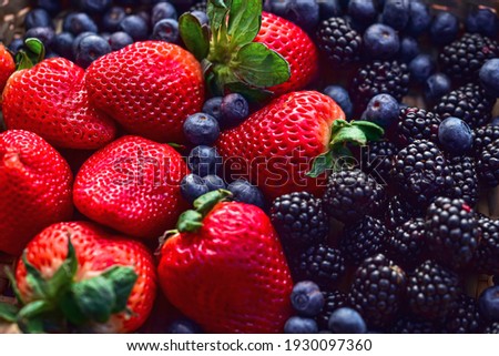 woven basket of red strawberries with green leafy tops, surrounded by ripe blackberries and blueberries Royalty-Free Stock Photo #1930097360