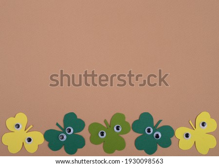 St Patricks Day paper shamrocks with cartoon plastic eyes on beige background.  Flat lay, top view.