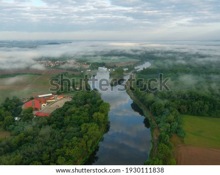 Weir with clouds reflection in the river in foggy rural area from the air